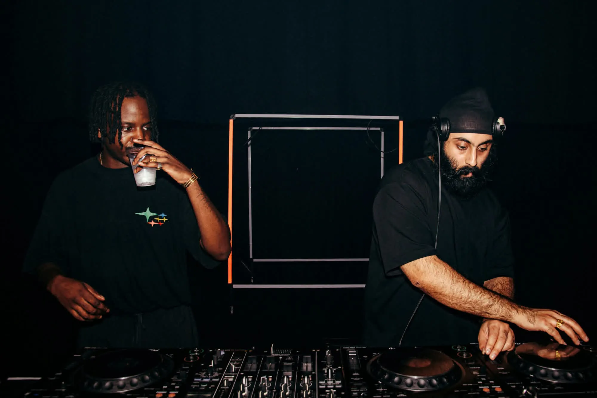 Salut and Yung Singh at the decks, a lit square frame behind them